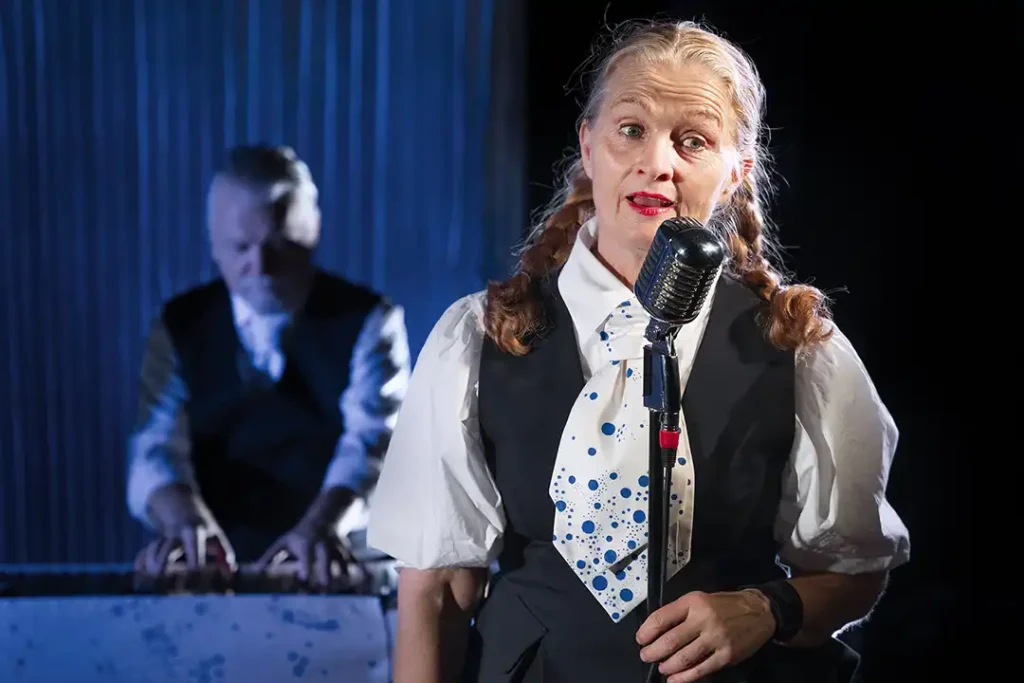 Baura L. Magnúsdóttir sjunger i bakgrunden en skådespelare spelar piano